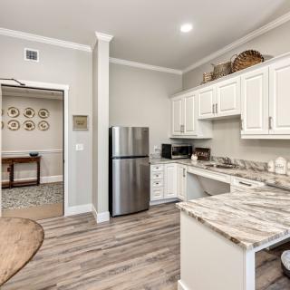 A modern kitchen with white cabinets, a stainless steel fridge, and hardwood flooring.