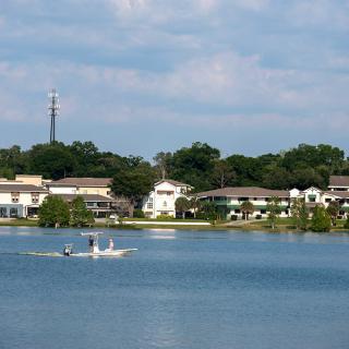 A serene lakeside view with houses in the background and people boating on the water.