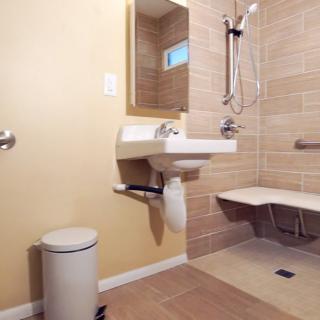 An accessible bathroom with a modern design, featuring a sink, shower with grab bars, and a wall-mounted mirror.