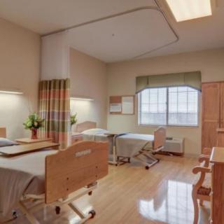 A clean and well-organized hospital room with two beds and wooden flooring.