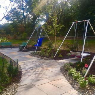 A sunny outdoor garden featuring a playground with swings and a paved pathway.