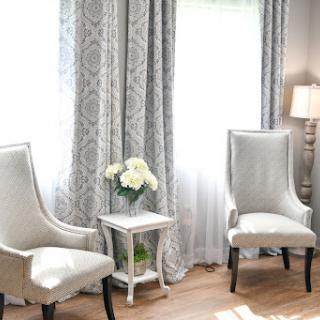 A cozy living room setup featuring elegant chairs, stylish curtains, and a touch of floral decor.