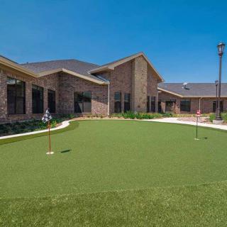 A modern building with a well-maintained putting green in the foreground under a clear blue sky.