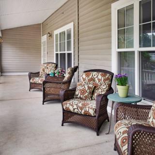 A cozy porch with wicker armchairs and floral cushions, accompanied by small tables and potted plants.
