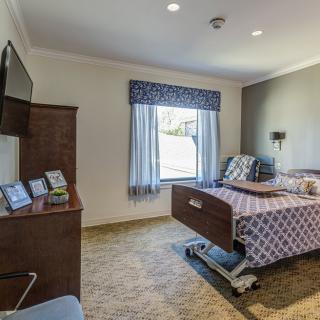 A well-furnished hospital room with a bed, television, and large window for natural light.