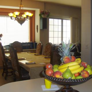 A dining room with a table set and a fruit bowl centerpiece, illuminated by a chandelier.