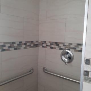 A modern shower with decorative tiles and grab bars.