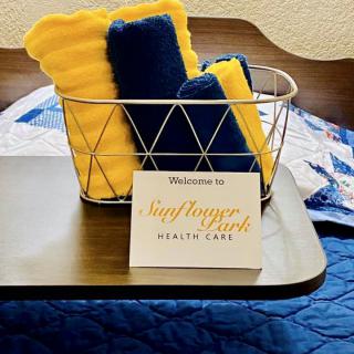 A wire basket with yellow and blue towels beside a welcome card on a bedside table.