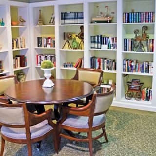 A cozy reading area featuring a round table, surrounded by bookshelves filled with books and decorative items.