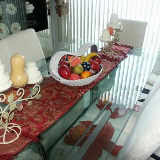 A dining table decorated with a fruit bowl and decorative candles on a patterned table runner.