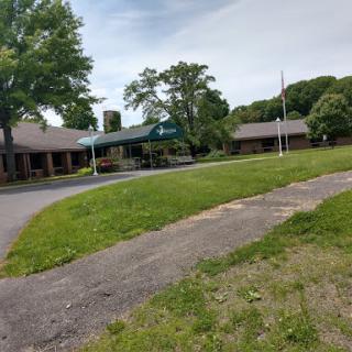A view of a well-kept building surrounded by lush green grass and trees, featuring a flagpole and a paved pathway.