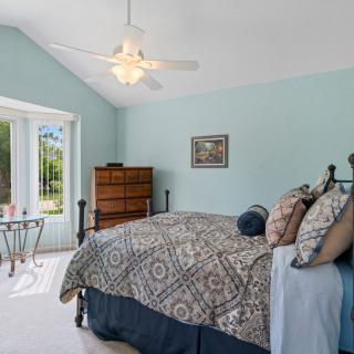 A cozy bedroom with a patterned bedspread, decorated in soothing colors and illuminated by natural light from a large window.