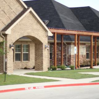 A suburban brick house with a well-manicured lawn and a shaded porch area.