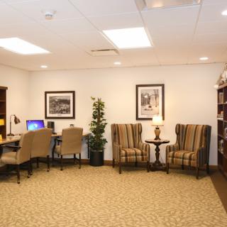 A cozy office lounge area featuring desks with computers, comfortable chairs, a bookshelf, and decorative artwork on the walls.