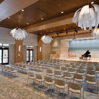 A modern auditorium with a grand piano on stage and rows of empty chairs.