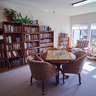 A cozy reading room with bookshelves, a table, and chairs by a window.