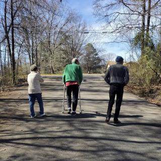 Three people walking on a path surrounded by trees.