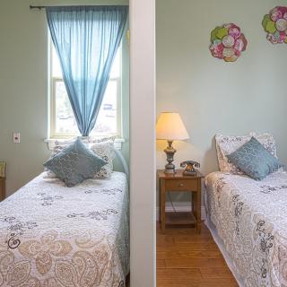 A cozy bedroom featuring twin beds with matching bedspreads, a small bedside table with a lamp, and decorative wall accents.
