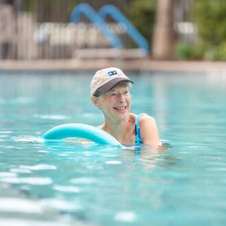 A person enjoys a relaxing day at the pool, using a foam noodle for support while swimming.