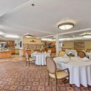 An elegant dining room with round tables and upholstered chairs, featuring a carpeted floor and chandeliers.