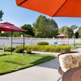 A sunny patio with red umbrellas, chairs, and well-maintained garden landscaping.