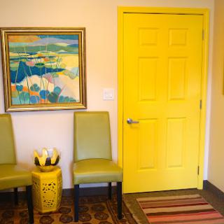 A vibrant interior space featuring a yellow door, green chairs, and a colorful piece of art.