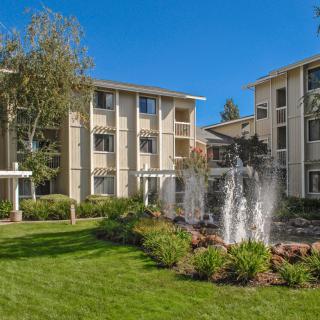 A view of a residential apartment complex with a fountain and landscaped gardens.