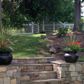 A serene garden with stone steps leading up to a white fence, flanked by planters.