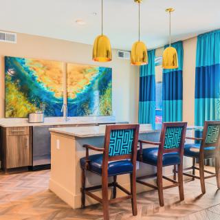 A modern kitchen with vibrant artwork, blue and yellow accents, featuring a sleek island and comfortable bar stools.