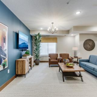 A modern living room with stylish furniture and decor, featuring a blue accent wall, comfortable seating, and a flat-screen TV.