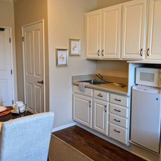 Compact kitchen space with white cabinets, a mini fridge, and microwave adjacent to a small dining area.