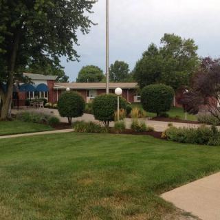 A well-manicured lawn with neatly trimmed bushes and trees, surrounding a building with a flagpole in the center.