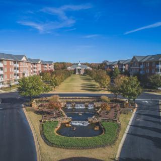 Aerial view of a landscaped residential complex with buildings, roads, and a central fountain.