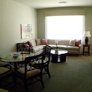 A cozy living room with a sofa, round table, chairs, and a large window.