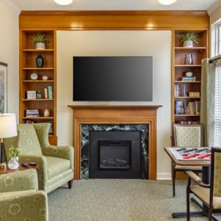 A cozy living room with a fireplace, television, and bookshelves surrounded by comfortable armchairs.
