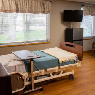 A hospital room featuring a bed, tray table, and television, with natural light coming through the windows.