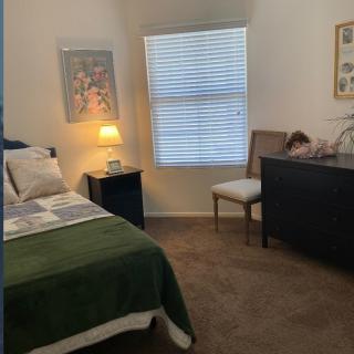 A cozy bedroom with a neatly made bed, nightstand with a lamp, and artwork on the walls.