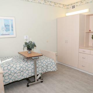 A clean and minimalist hospital room featuring a bed, wardrobe, and bedside table.