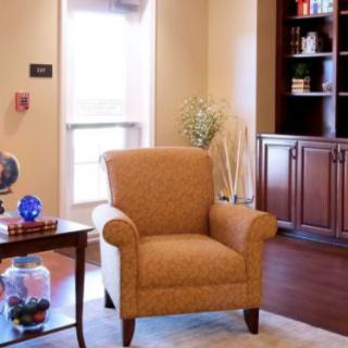 A cozy living room with an armchair, a small table with decorations, and a bookshelf.
