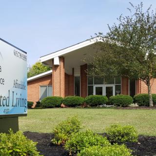 A brick building with a sign indicating it is an assisted living facility, surrounded by landscaping.