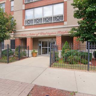 A view of an apartment building entrance with a small garden and sidewalk.
