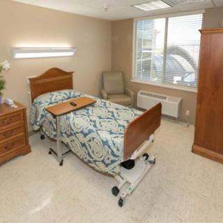 A clean and organized hospital room with a single bed, bedside cabinet, and chair.