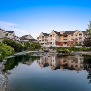 A serene residential complex with apartments overlooking a tranquil lake and lush greenery.