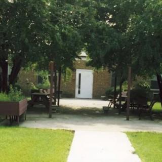 A peaceful garden pathway lined with benches and trees leading to a building entrance.