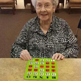An elderly woman smiles while playing a game of bingo indoors.