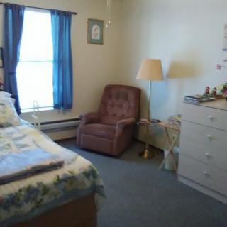 A cozy bedroom with a bed, armchair, and a dresser near a window with blue curtains.