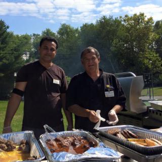 Two people cooking at an outdoor barbecue event.