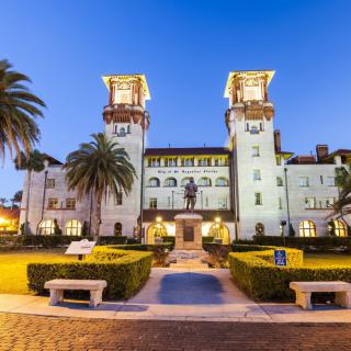 A beautifully illuminated historic building with twin towers and palm trees at night.
