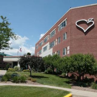 A brick hospital building with a heart symbol on the facade, surrounded by trees and landscaping.