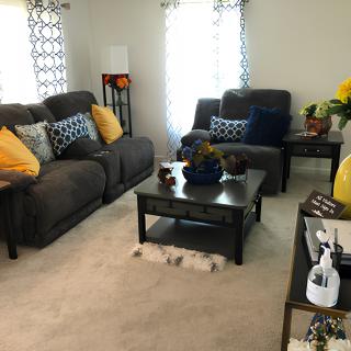 A cozy living room with dark sofas, colorful cushions, and a central coffee table.